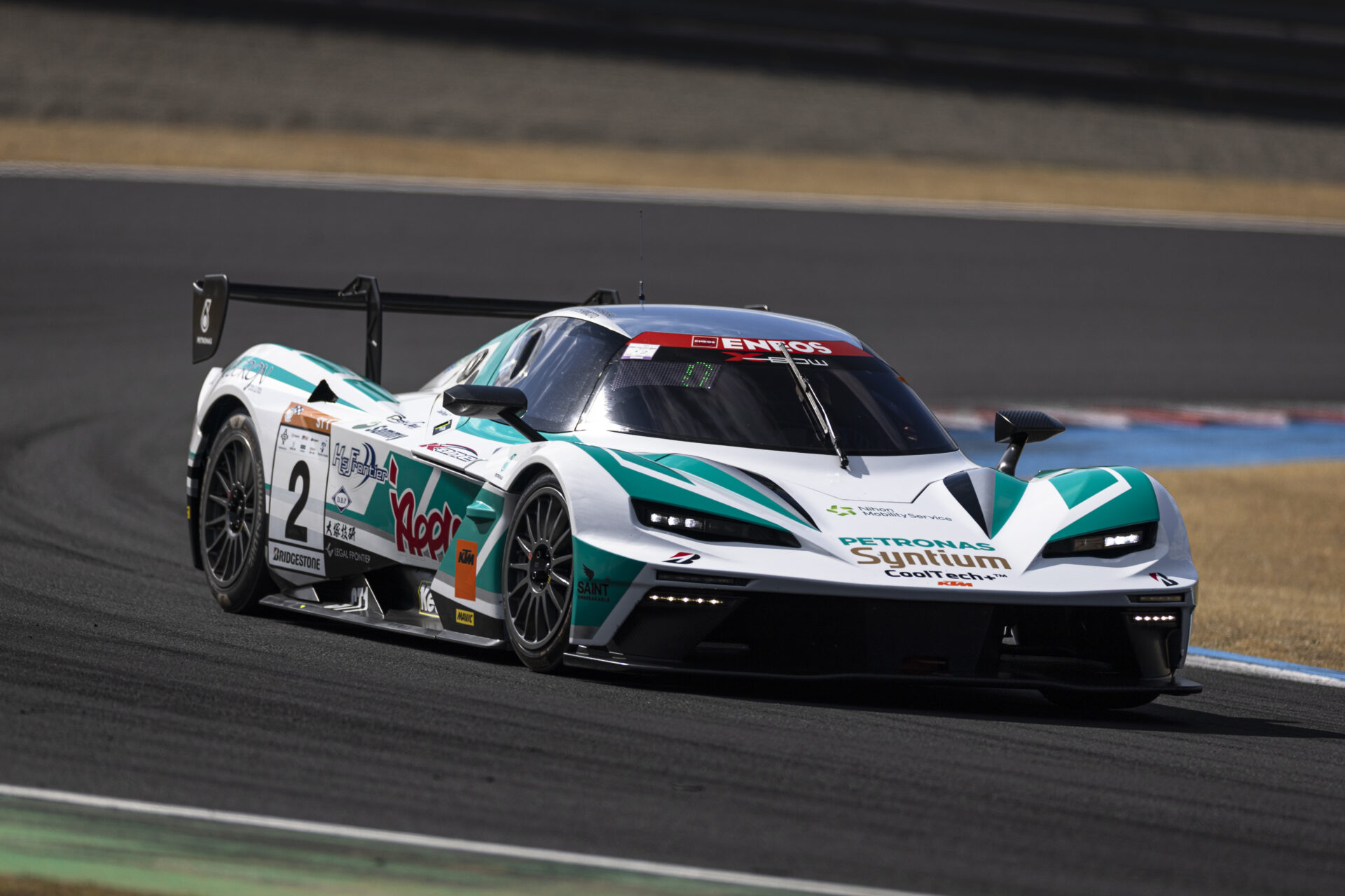 White race car with teal and green accents speeding on a race track, sponsor logos visible and number 2 on the side.